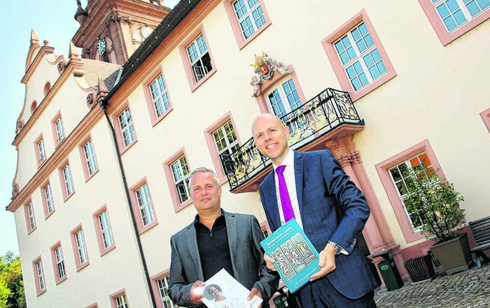 Zwei Männer stehen vor dem Kloster und halten Broschüren in den Händen
