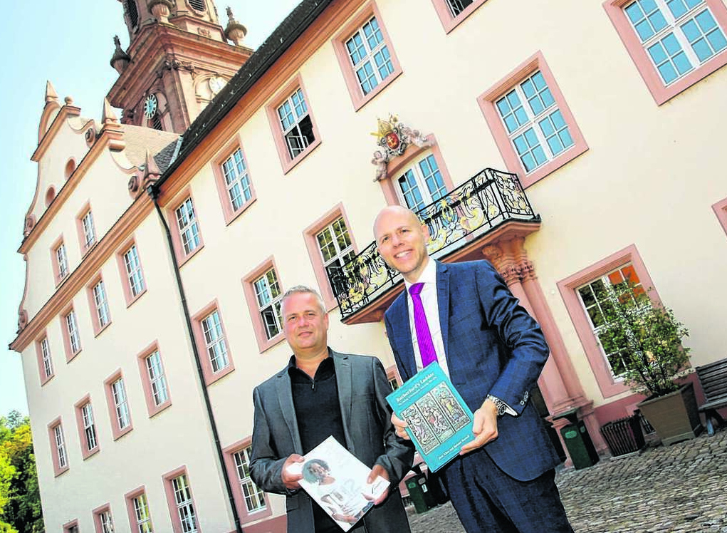 Zwei Männer stehen vor dem Kloster und halten Broschüren in den Händen